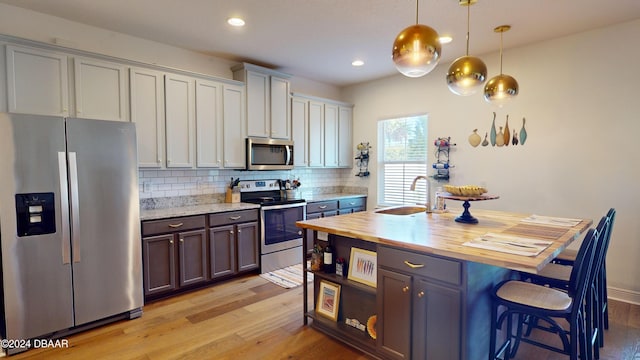 kitchen with wood counters, backsplash, sink, appliances with stainless steel finishes, and decorative light fixtures