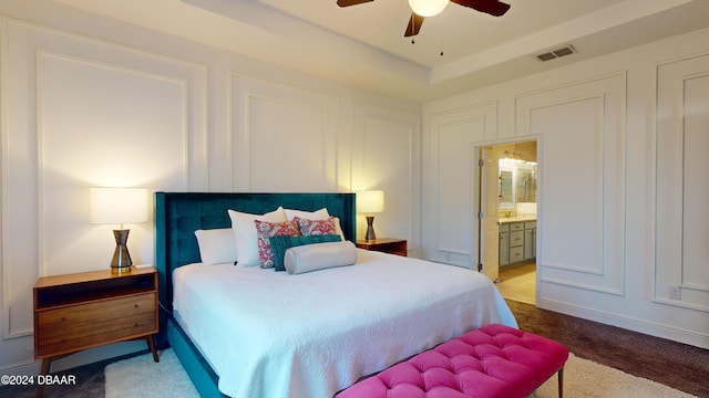 bedroom featuring carpet floors, ensuite bathroom, a raised ceiling, and ceiling fan