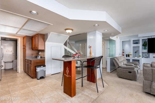 kitchen featuring light tile patterned floors, stainless steel fridge, a kitchen bar, and kitchen peninsula