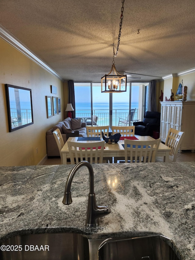 interior space featuring sink, a water view, a notable chandelier, ornamental molding, and a textured ceiling