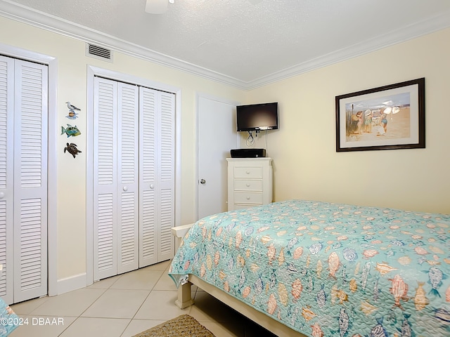 bedroom featuring two closets, crown molding, and light tile patterned flooring