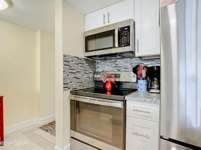 kitchen featuring stainless steel appliances, light tile patterned floors, white cabinets, and backsplash