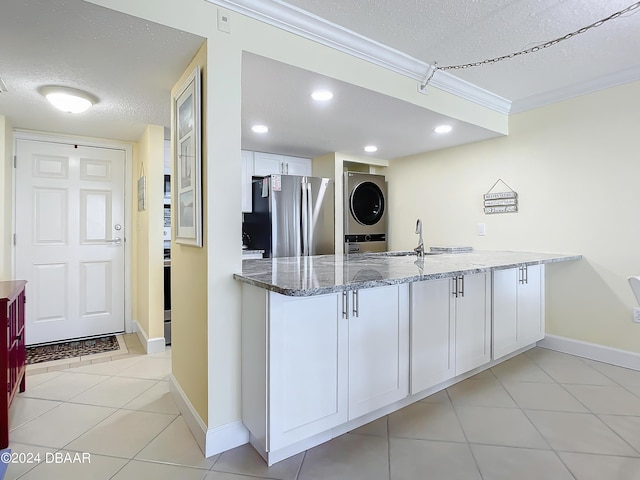 kitchen featuring stacked washer / drying machine, white cabinetry, a textured ceiling, stainless steel fridge, and stone counters