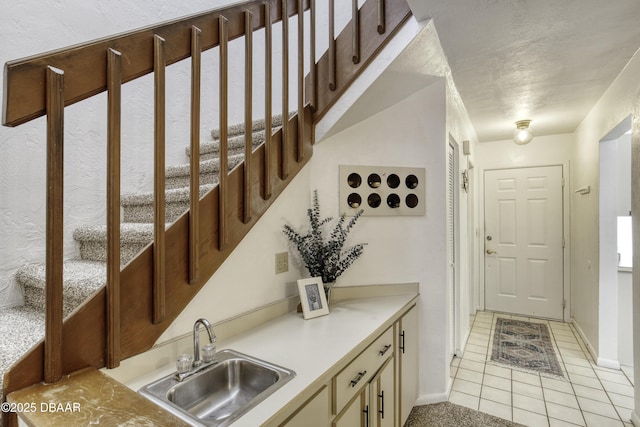 kitchen with a sink, baseboards, light tile patterned floors, light countertops, and a textured ceiling