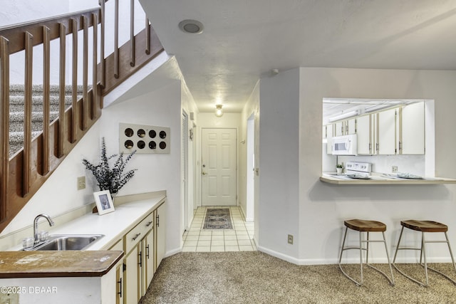 kitchen featuring a sink, white appliances, light colored carpet, and a peninsula
