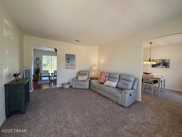 carpeted living room with ceiling fan with notable chandelier