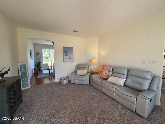 living room featuring ceiling fan, a textured ceiling, and dark colored carpet