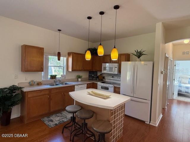 kitchen with pendant lighting, a center island, white appliances, a kitchen breakfast bar, and dark hardwood / wood-style flooring