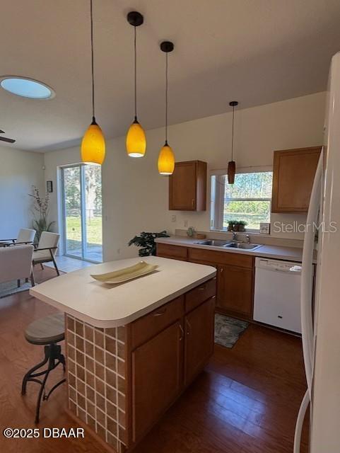 kitchen with sink, dark wood-type flooring, decorative light fixtures, white appliances, and a kitchen island