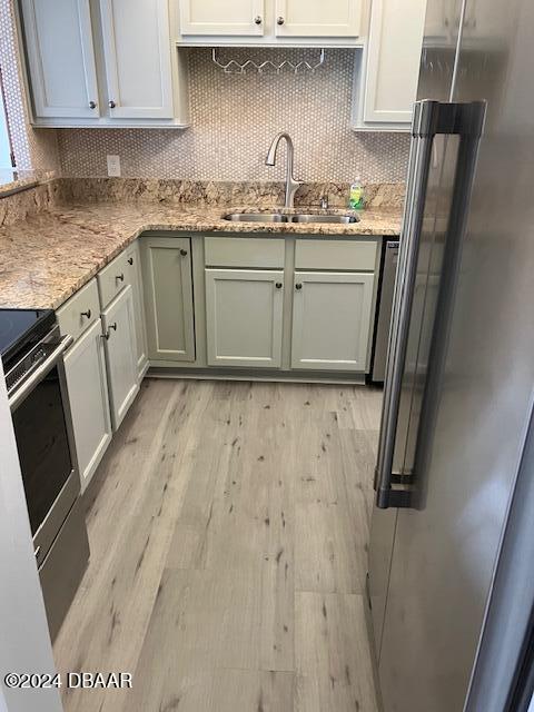 kitchen featuring sink, light stone counters, decorative backsplash, appliances with stainless steel finishes, and light wood-type flooring