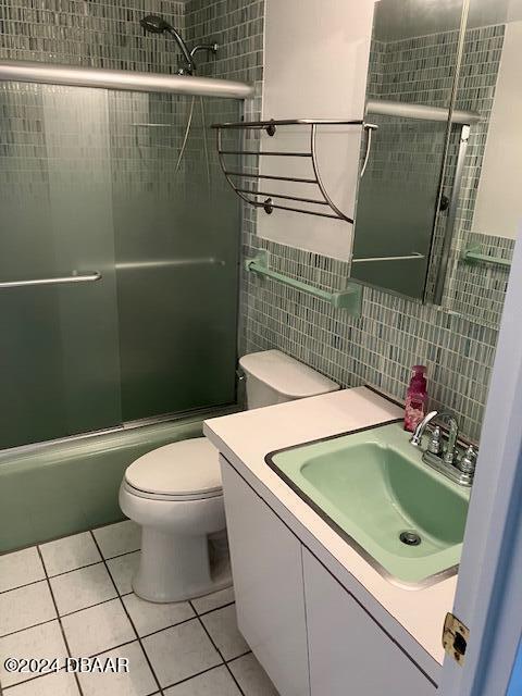 full bathroom featuring tile patterned floors, vanity, shower / bath combination with glass door, tile walls, and toilet