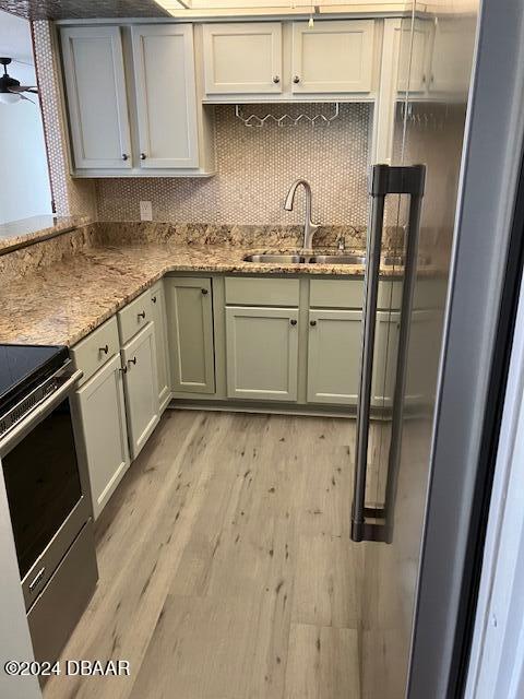 kitchen with sink, electric range, decorative backsplash, light stone countertops, and light hardwood / wood-style floors