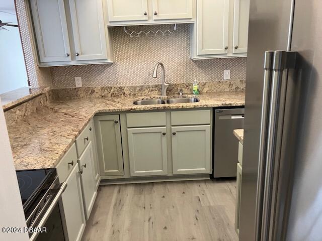 kitchen featuring decorative backsplash, light stone counters, stainless steel appliances, sink, and light hardwood / wood-style floors