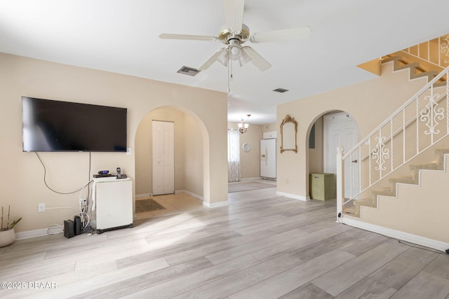 unfurnished living room featuring ceiling fan with notable chandelier and light wood-type flooring