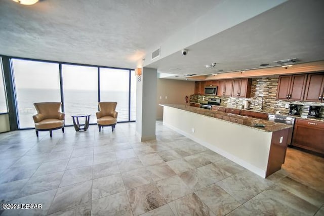 kitchen with tasteful backsplash, appliances with stainless steel finishes, floor to ceiling windows, dark stone countertops, and a water view