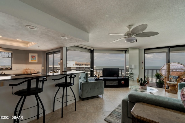 tiled living room with expansive windows, a tray ceiling, a textured ceiling, and ceiling fan