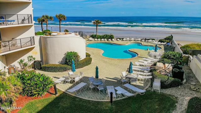 view of swimming pool with a patio, a water view, and a view of the beach