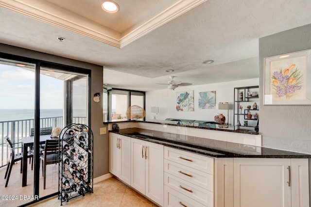 kitchen featuring white cabinetry, a water view, dark stone counters, ceiling fan, and light tile patterned floors