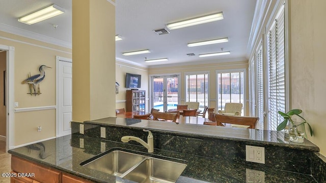kitchen featuring a sink, ornamental molding, brown cabinets, dark stone counters, and french doors