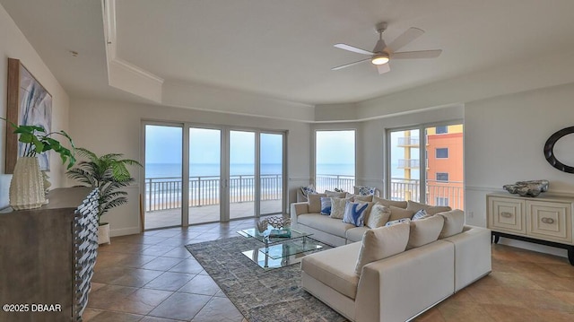 tiled living area featuring a ceiling fan, a water view, and a raised ceiling