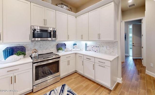 kitchen with light countertops, appliances with stainless steel finishes, light wood finished floors, white cabinetry, and visible vents