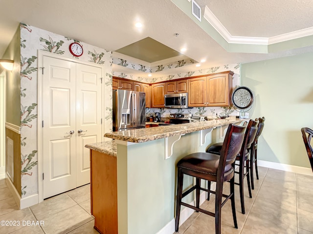 kitchen featuring appliances with stainless steel finishes, light stone countertops, a kitchen bar, a textured ceiling, and crown molding