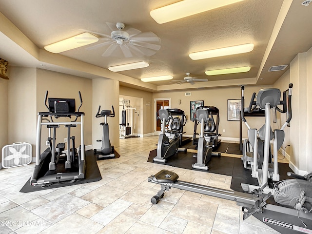 gym featuring a textured ceiling, ceiling fan, and a tray ceiling