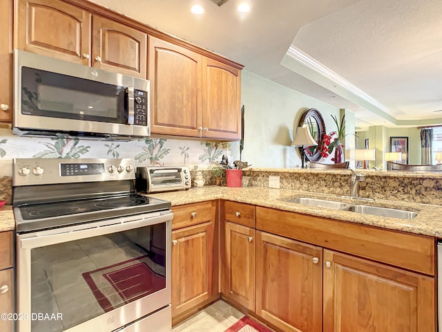 kitchen with light stone counters, ornamental molding, stainless steel appliances, sink, and a tray ceiling