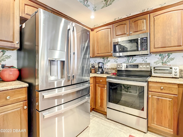2403 S Atlantic Ave Unit 409, Daytona Beach Shores, FL 32118 - kitchen with appliances with stainless steel finishes, light tile patterned flooring, brown cabinetry, and light stone countertops