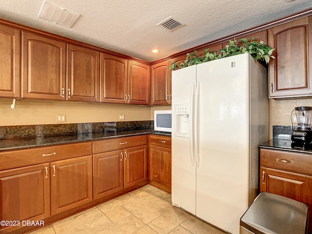 kitchen with white fridge with ice dispenser, dark stone counters, a textured ceiling, and light tile patterned flooring