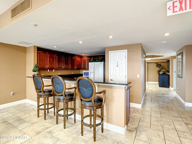 kitchen with a breakfast bar, white fridge with ice dispenser, and kitchen peninsula