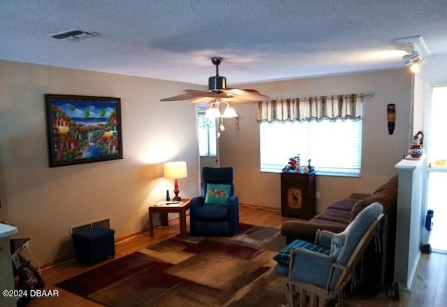 living room featuring hardwood / wood-style flooring, ceiling fan, and a textured ceiling