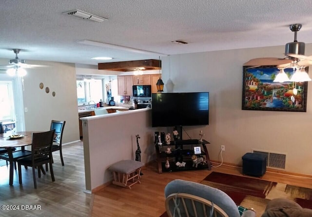 living room featuring ceiling fan, light wood-type flooring, and a textured ceiling