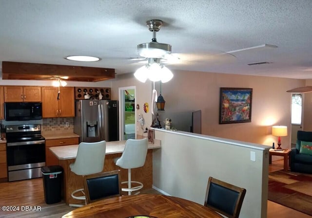 kitchen featuring a center island, dark wood-type flooring, tasteful backsplash, a breakfast bar area, and appliances with stainless steel finishes