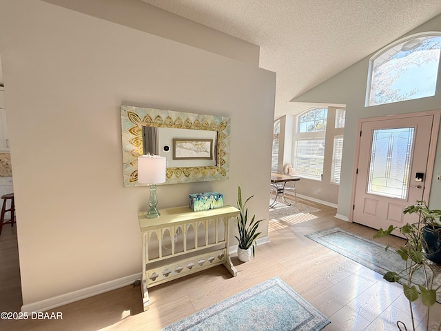 foyer entrance with a textured ceiling, light hardwood / wood-style floors, and high vaulted ceiling