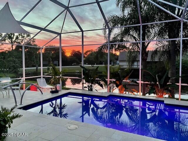 pool at dusk featuring glass enclosure and a patio area