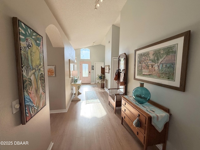 corridor with a textured ceiling, light hardwood / wood-style flooring, and high vaulted ceiling