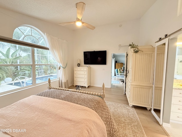 bedroom featuring ensuite bath, ceiling fan, a barn door, light wood-type flooring, and a textured ceiling