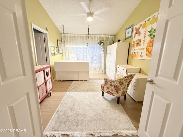 living area with ceiling fan, lofted ceiling, a textured ceiling, and light hardwood / wood-style flooring