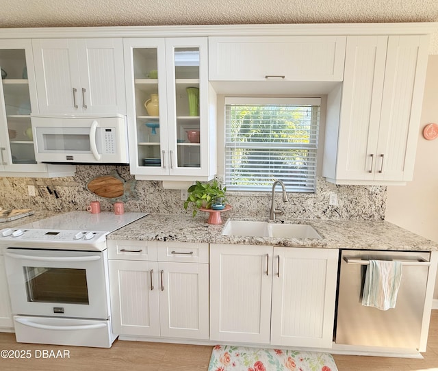 kitchen with white cabinets, white appliances, light stone counters, and sink