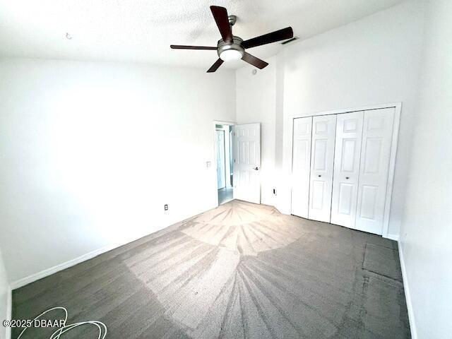 unfurnished bedroom featuring ceiling fan, a towering ceiling, a textured ceiling, and a closet