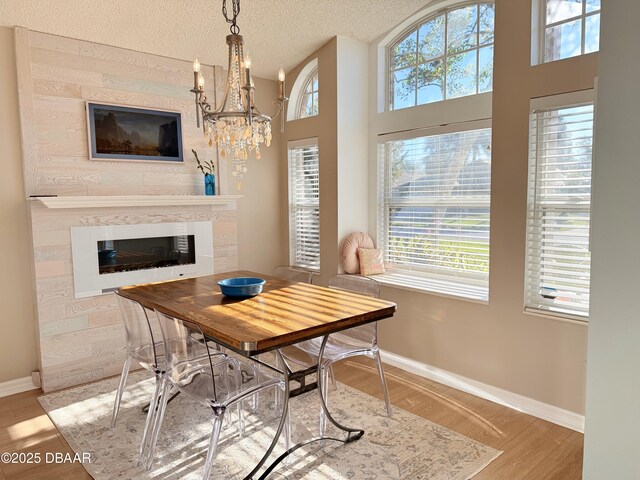 dining area with a chandelier, a large fireplace, a textured ceiling, and light hardwood / wood-style flooring