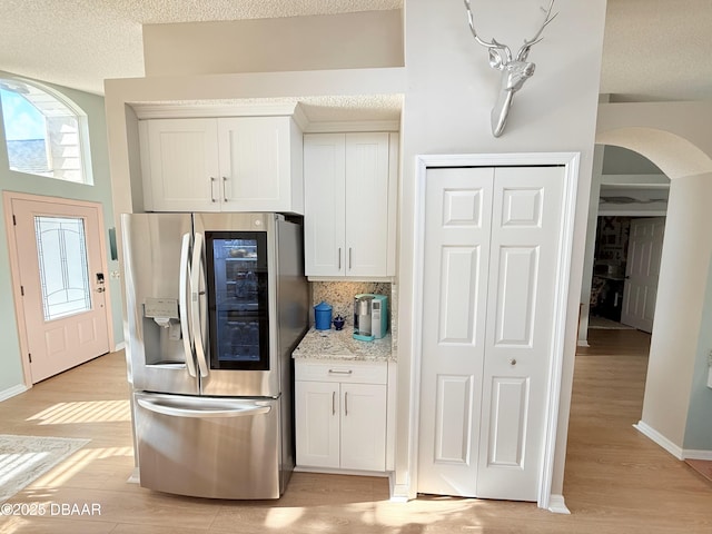 kitchen featuring stainless steel refrigerator with ice dispenser, tasteful backsplash, light hardwood / wood-style floors, light stone counters, and white cabinetry