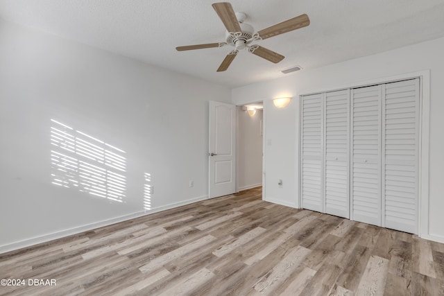 unfurnished bedroom with a textured ceiling, light hardwood / wood-style flooring, ceiling fan, and a closet