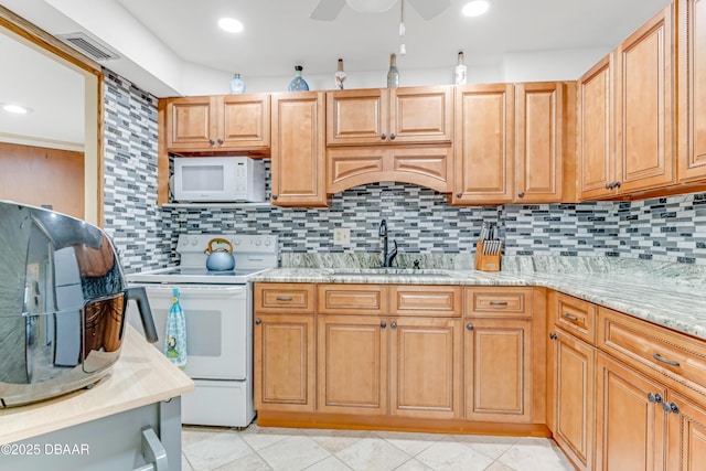 kitchen featuring tasteful backsplash, light stone countertops, light tile patterned floors, white appliances, and a sink