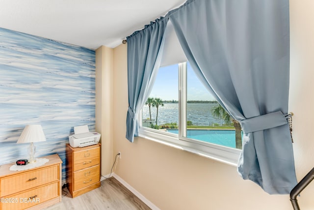 bedroom with light wood-style floors, wallpapered walls, an accent wall, and baseboards