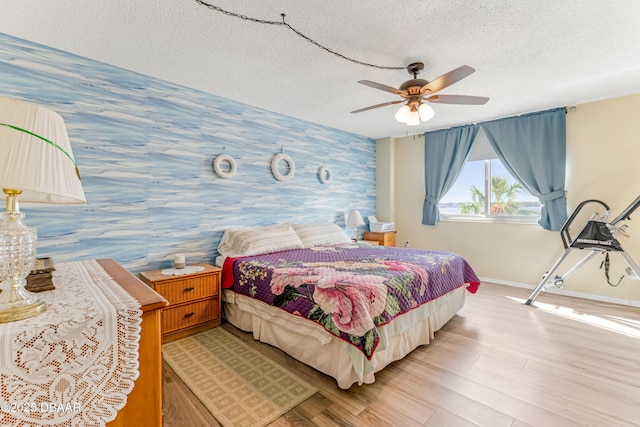 bedroom with a textured ceiling, light wood-style floors, wallpapered walls, baseboards, and an accent wall