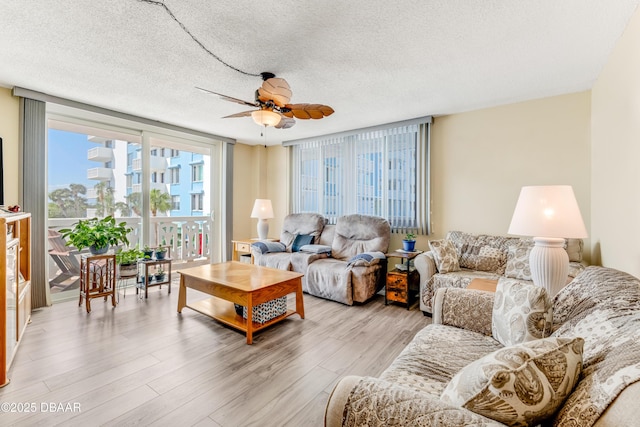 living area featuring light wood-style floors, ceiling fan, and a textured ceiling