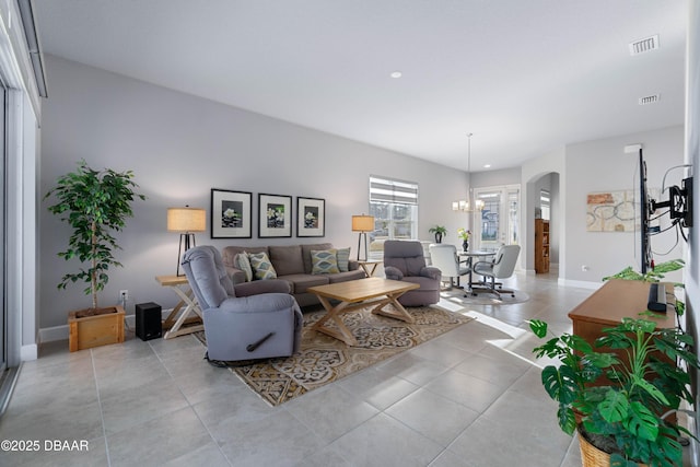 living area with arched walkways, visible vents, light tile patterned flooring, a chandelier, and baseboards