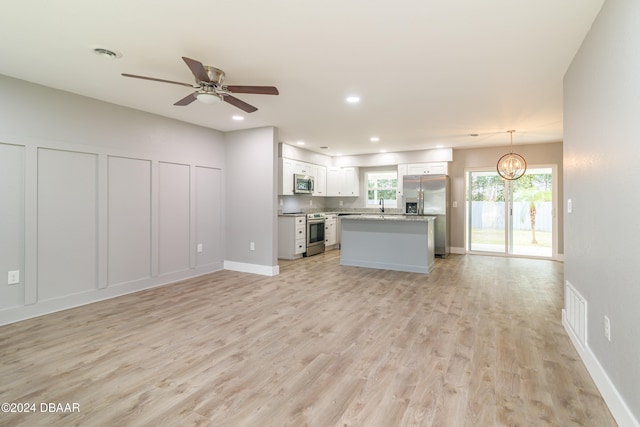 unfurnished living room with ceiling fan with notable chandelier, sink, and light wood-type flooring